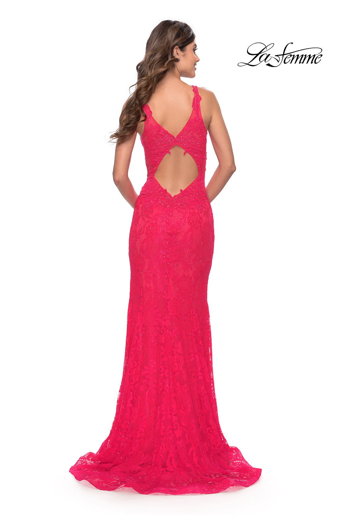 A woman stands facing away in a bright pink La Femme 29978 deep V-neck long lace prom dress with a cutout back. The La Femme logo is in the top right corner.